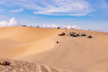 Fototapeta na wymiar Sand dunes near Mui Ne. Group of jeeps on top of dunes in the background. Sunny day with blue sky and clouds.