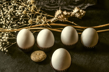 White eggs in brown corrugated paper capsule with dry white flowers on a black background