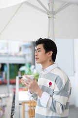 Handsome young man drinking coffee looking out at the view on balcony