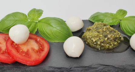Italian Caprese salad with mini mozzarella balls, tomato, green pesto and basil
