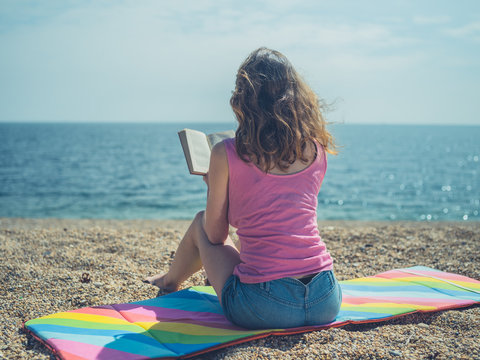 Young woman sitting on beach reading a book in summer