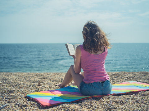Young woman sitting on beach reading a book in summer