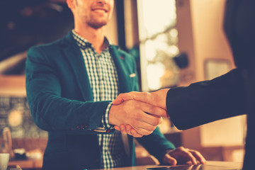 Two businessman shaking hands in a cafe. Focus on hands
