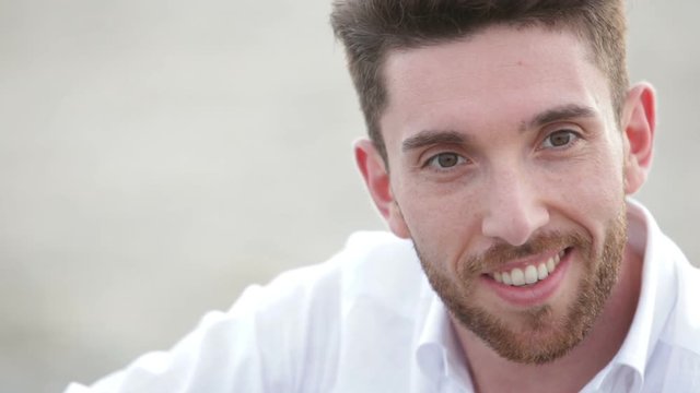Sorriso di un ragazzo felice seduto sulla spiaggia in estate con una Camicia bianca. 
