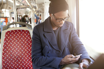 Portrait of serious African American hipster in black stylish hat and coat using smartphone sitting...