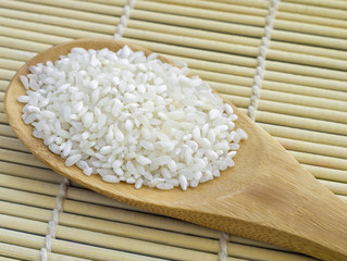 Rice in a wooden spoon on bamboo table-napkin. Selective focus.