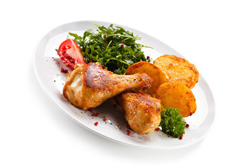 Roast chicken drumsticks with potatoes on white background
