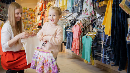 Fototapeta na wymiar Young mother with blonde daughter buying kids clothes in store