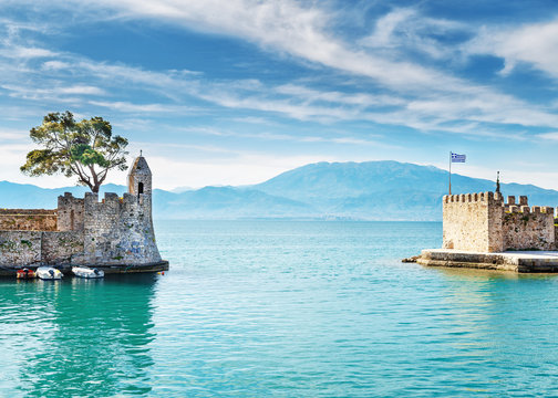 Amazing morning scenery of old port gate in Nafpaktos town, Western Greece, nearby Patras city. Beautiful dramatic blue sky at background. Turquoise water of Ionian sea. Vintage style scenery.