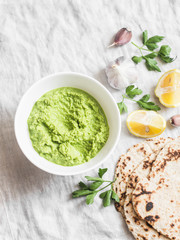 Green avocado dip and gluten free flatbread on a light background, top view. Healthy vegetarian snack
