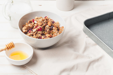 Morning granola with dried fruits, honey, milk and berries on white wooden background. Side view iwth copy space