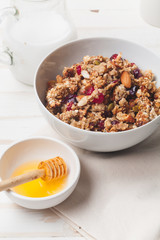 Morning granola with dried fruits, honey, milk and berries on white wooden background. Side view, close up