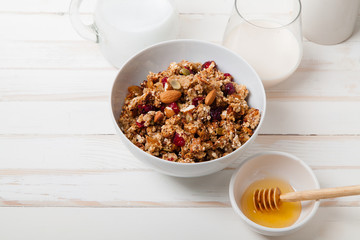 Morning granola with dried fruits, honey, milk and berries on white wooden background. Top view with copy space