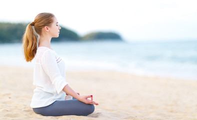 Fototapeta na wymiar woman practices yoga and meditates in lotus position on beach.