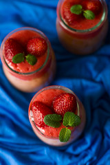 Fresh strawberry and banana smoothies decorated berry and mint leaves on blue napkin. Selective focus