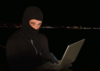 Criminal in hood on laptop in front of night lights