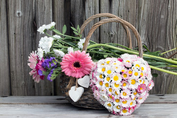 Fototapeta na wymiar Herz aus Gänseblümchen und einem Weidenkorb mit buntem Blumenstrauß