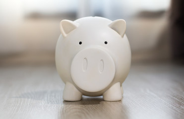 White piggy saving money with coin on wooden floor.