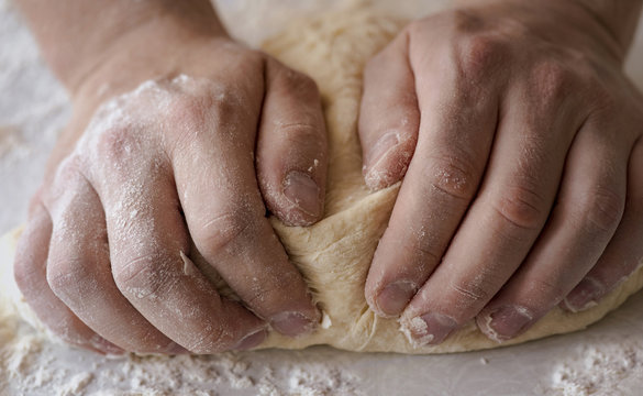 Close-up male hands kneading dough on sprinkled with flour table