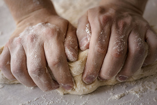 Close-up male hands kneading dough on sprinkled with flour table