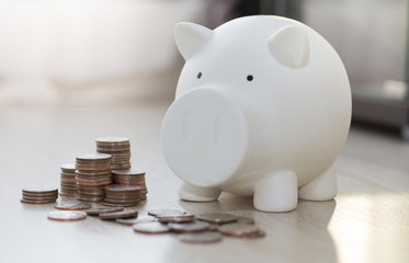 White piggy saving money with coin on wooden floor.