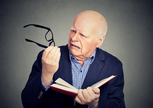 Elderly man holding book, glasses having eyesight problems unable to read
