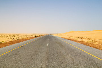 Fototapeta na wymiar Well paved and seemingly endless road leading through dunes in the dry and hot desert are part of the transportation infrastructure of the Sultanate of Oman on the Arabian peninsula in the Middle East