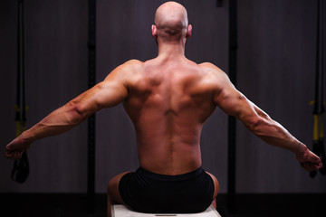 Fototapeta na wymiar Young healthy bald ripped man with big muscles posing in gym, view from the back