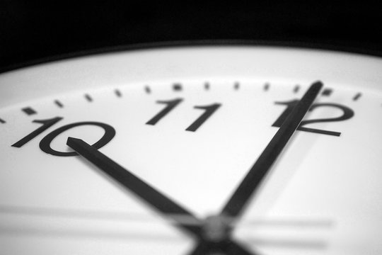 Closeup on the pointers of a clock marking a few seconds before ten o’clock - black and white rendering. The main focus is on the number ten and its pointer. - Powered by Adobe