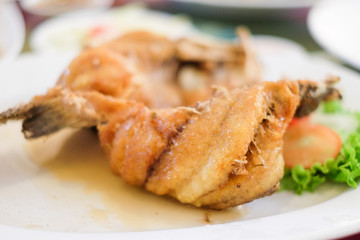 Deep fried snapper topped with sweet fish sauce and vegetable serve on white dish.