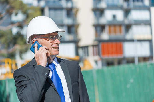 Man architector outdoor at construction area having mobile conversation