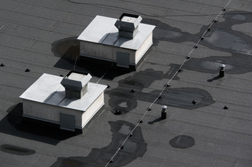 Lines of grey and black asphalt on the flat roof. Cables and devices of ventilation and airing on...