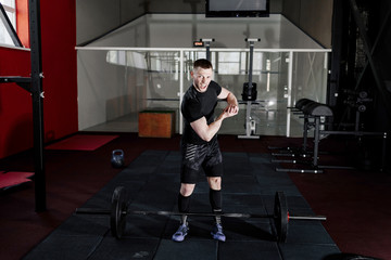 Fototapeta na wymiar Screaming young man dressed in black t-shirt showing his biceps in gym. Man posing in gym and looking at camera while showing his biceps