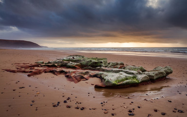 sunset on the Atlantic coast overlooking a huge beautiful boulder under storm clouds