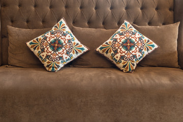 The beautiful vintage fabric two pillows on luxurious brown leather sofa interior decoration