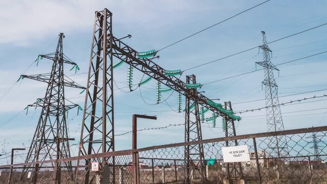 High-voltage electrical substation. Pylons with insulators and wires behind a protective fence. Electric and power industry. Production of electricity and transporting it to cities. Generators and