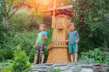 Obraz premium Two boys next to small mill in summer city park in sunlight