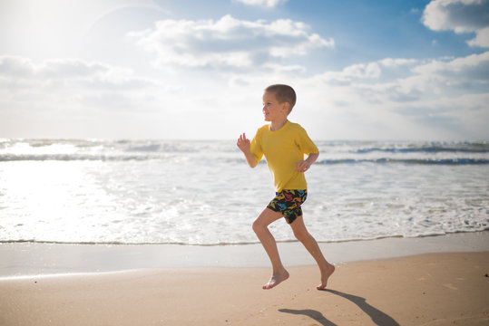 Boy in shorts and a yellow T-shirt runs along the sea