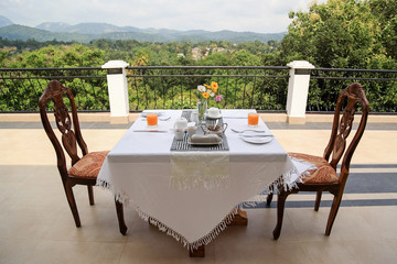Breakfast table covered with white cloth, prepared for breakfast, outdoor on balcony with a view on the green nature in Sri Lanka