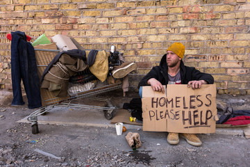  Homeless man sitting on the street, with cardboard. Homeless, please help - sign on the cardboard.
