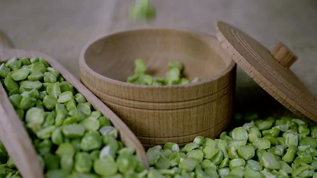 Granules of green peas fall into a wooden bowl. Slow motion. close-up