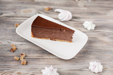 A slice of a chocolate cheese cake on a wooden background with some cane sugar cubes around. Low depth.