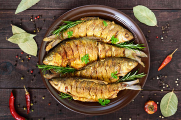 Fried fish carp (sazan) on a ceramic bowl with branches of rosemary on a dark wooden background....