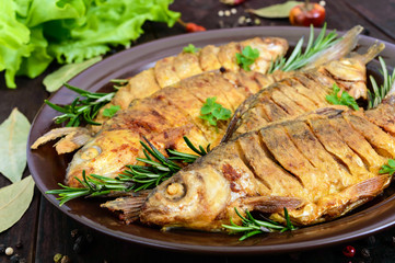 Fried fish carp (sazan) on a ceramic bowl with branches of rosemary on a dark wooden background. Close up