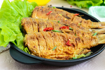 Fried fish carp (sazan) on a cast-iron frying pan with lettuce leaves on a light background. Close up