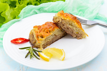 Juicy meat cutlet, baked with grated potatoes and cheese on a white ceramic plate on a light background. Close up