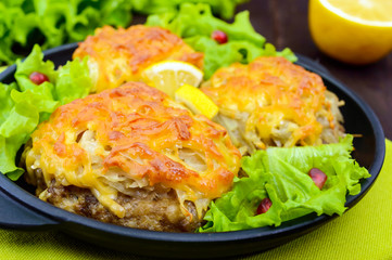 Juicy meat cutlet, baked with grated potatoes and cheese on a cast-iron frying pan on a dark wooden background. Close up