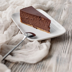 A slice of a chocolate cheese cake on a wooden background with some cane sugar cubes around. Low depth.