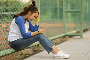 Woman sad looking in message on mobile a bad news by sit beside tennis court outdoor
