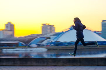 Silhouettes a young man on a run in the city on the embankment during sunset. Blur in motion abstract image of a man's silhouette